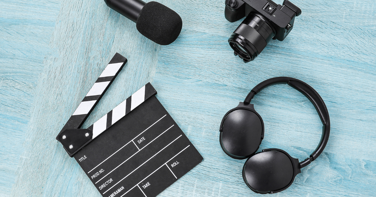 A black film clapperboard, headphones, a microphone, and a camera are arranged on a light blue wooden surface—perfect tools for applying your brand to content with style and creativity.