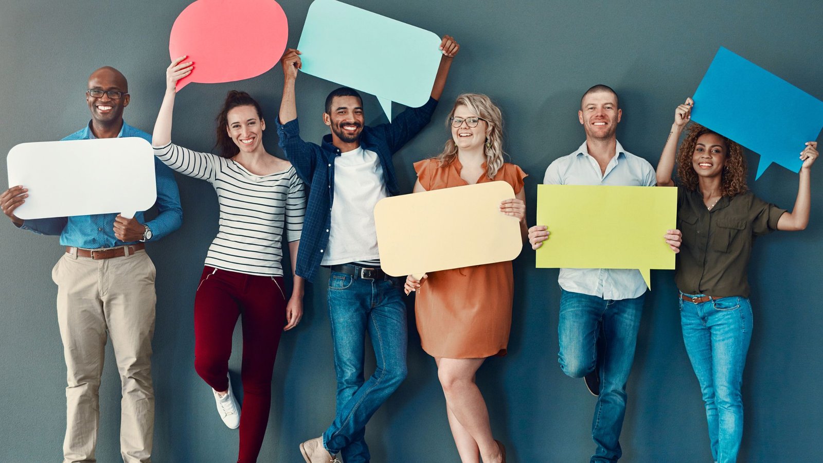 A line of Adults against a medium blue wall holding various colored speech bubbles as a representation of brand voice and messaging